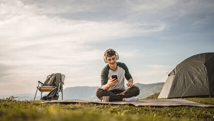 Young boy sit on blanket on the mountain listen music on headphones