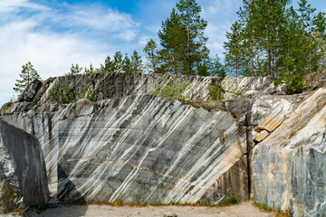 Scenic view of a marble quarry with distinct striations and pine trees in the background. The image...