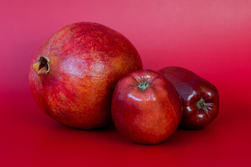Ripe pomegranates and apples on a red background.