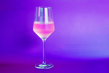 pink wine in a glass on a purple background with copy space