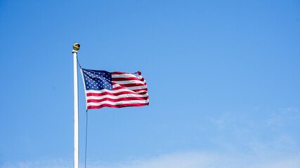 A photograph of the American flag waving proudly in the wind against a backdrop of a clear blue sky.