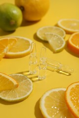 Skincare ampoules with vitamin C and citrus slices on yellow background