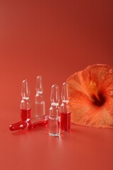 Skincare ampoules and hibiscus flower on coral background