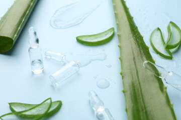 Skincare ampoules with extract of aloe vera and green leaves on light blue background, closeup