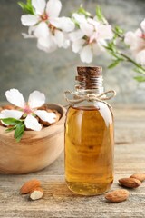 Almond oil in bottle, flowers and nuts on wooden table, closeup