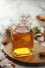 Almond oil in bottle, nuts and flowers on white table, closeup