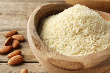 Fresh almond flour in bowl and nuts on wooden table, closeup