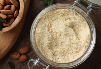 Fresh almond flour in jar and nuts on wooden table, flat lay