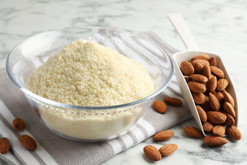 Fresh almond flour in bowl, scoop and nuts on white marble table, closeup