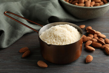 Fresh almond flour in scoop and nuts on wooden table, closeup