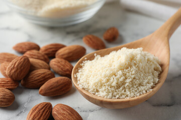 Spoon with fresh almond flour and nuts on white marble table, closeup