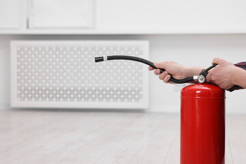 Man with fire extinguisher indoors, closeup. Space for text