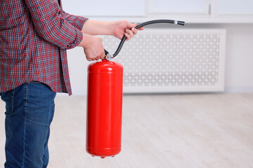 Man with fire extinguisher indoors, closeup. Space for text