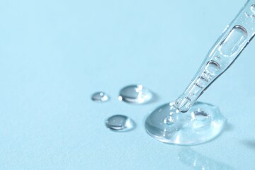 Glass pipette and transparent liquid on light blue background, closeup. Space for text