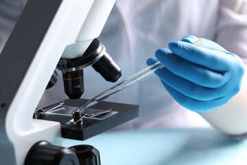 Doctor dripping liquid from pipette onto glass slide on microscope, closeup. Laboratory analysis