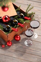 Wooden crate with bottles of wine, glasses, fir twigs and red Christmas balls on table