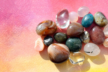 Colorful semi-precious stones illuminated by sunlight lie on a bright pink background. Healing crystals.