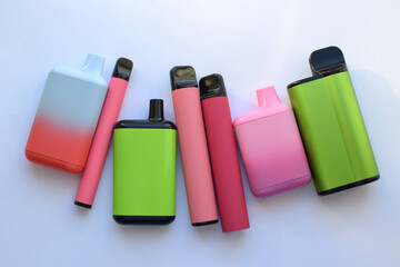 Several multi-colored electronic cigarettes lie on a light table. © Oksana