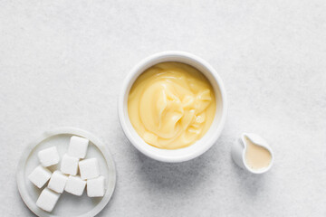 Overhead view of nigerian akamu in a white bowl with sugar and milk, pap akamu or ogi in a white bowl, top view of nigerian corn pudding in a white ramekin