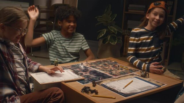 Medium shot of group of multiracial kids gathered to play board game at home in evening and putting hands together for lucky game