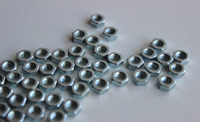 Many same iron nuts are tightly fitted to each other in an abstract shape on a white table 