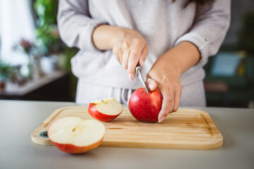 An unknown adult woman stand and cut apple with knife on table