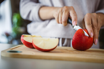 An unknown adult woman stand and cut apple with knife on table