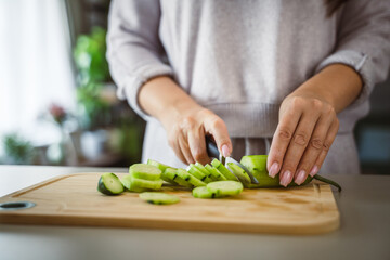 An unknown adult caucasian woman stand and cut cucumber at home