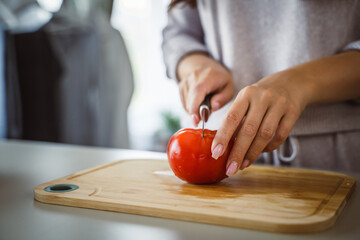 An unknown woman stand and cut tomato with knife on table at home
