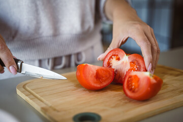 An unknown woman stand and cut tomato with knife on table at home