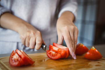 An unknown woman stand and cut tomato with knife on table at home