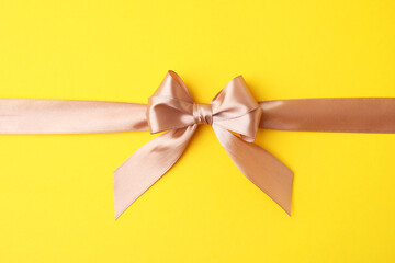 Fototapeta premium Beige satin ribbon with bow on yellow background, top view