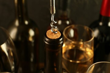 Wine bottle with corkscrew on blurred background, closeup