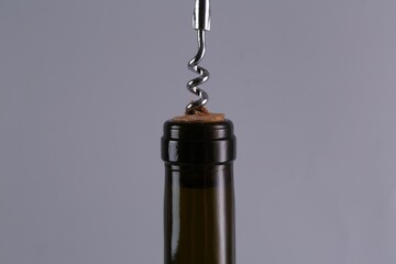 Wine bottle with corkscrew on grey background, closeup