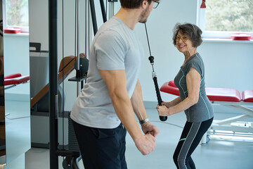 Smiling pensioner performs rehabilitation exercises on a simulator