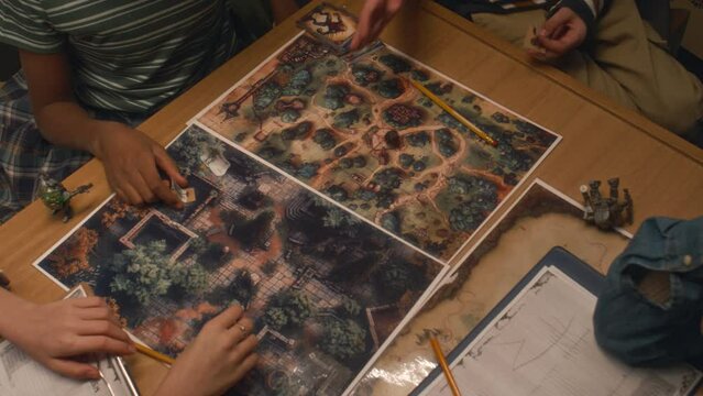 Overhead shot of faceless children rolling dice and making moves with cardboard figures in turn. Process of playing table game at home