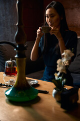Elegant asian woman enjoying strong tea and flavored hookah