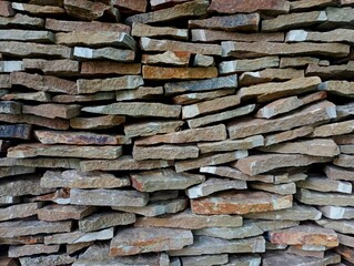 Large flat stone blocks of sandstone are stacked on top of each other and form a wall of stone rows. Natural building materials are stacked. Beautiful natural building textures.