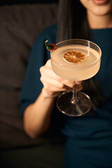 Woman holding cocktail decorated with slices of chilly pepper and dried orange