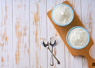 Greek yogurt or sour-cream in a blue ceramic bowl on a white table, top view.