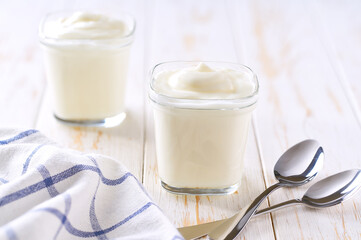Two portions of natural organic yogurt in a glass jars on a white table, selective focus.