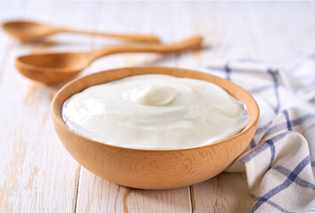 homemade organic yogurt in a wooden bowl with spoon on a white table, selective focus.