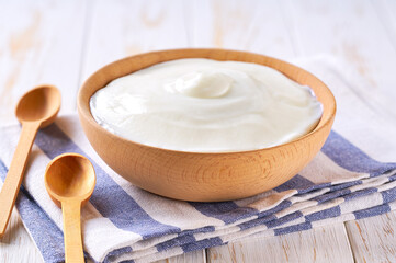 homemade organic yogurt in a wooden bowl with spoon on a white table, selective focus.