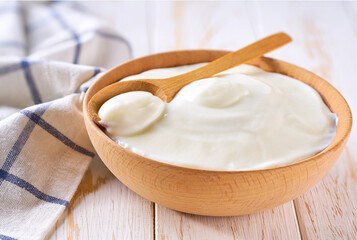 Natural yogurt in a wooden bowl with spoon on a light background, selective focus.