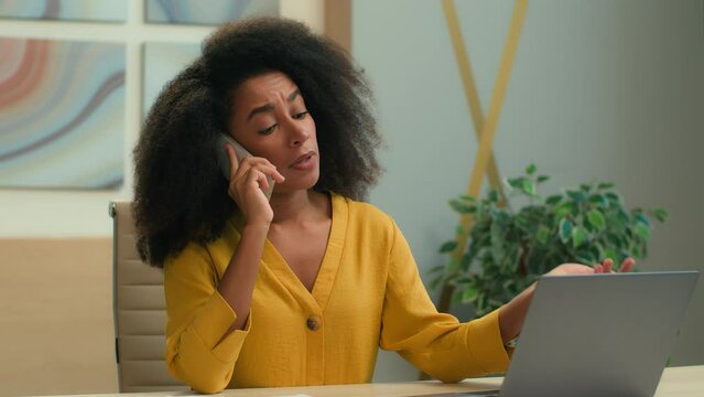 Sad upset woman African American businesswoman at office table manager business employer ceo female girl talk mobile phone worried displeased consult client speak working laptop answer smartphone call