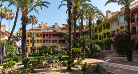 colorful building with red, yellow, and green facades under a clear blue sky. Palm trees and...