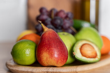 There are various fruits, apples, pears, grapes and avocados on a wooden plate