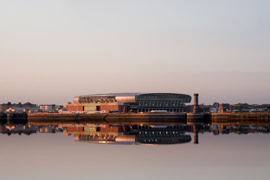 Liverpool, UK, June 2024: Liverpools historic waterfront with detail of Everton football clubs new bramley Moore dock premier league soccer stadium during sunset with reflection in mersey river