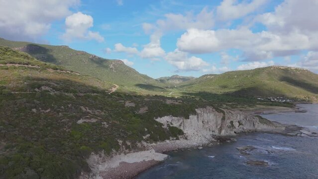 Drone flies towards rugged, rocky, Sardinian coastline in atmospheric light