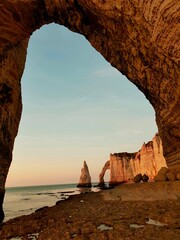 Felsen von Étretat bei Sonnenuntergang, Blick auf die Felsformation und Steilküste durch ein Felsentor, Frankreich © Emjoke